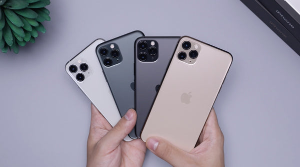 Hands holding four iPhones in varying neutral shades.