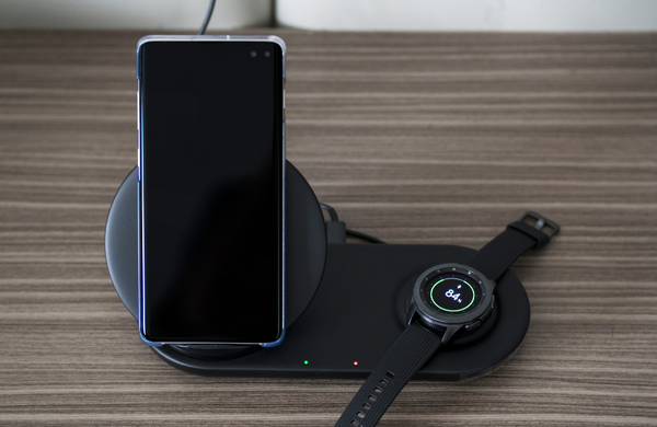 A smartphone and a smartwatch wirelessly charging on a wooden desk.