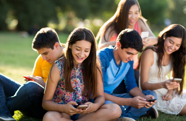 A group of teenagers sitting on grass all looking down at their phones.