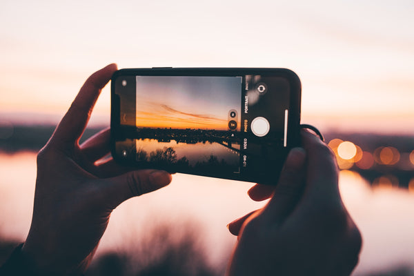 A phone with the camera app open pointed towards a sunset city skyline