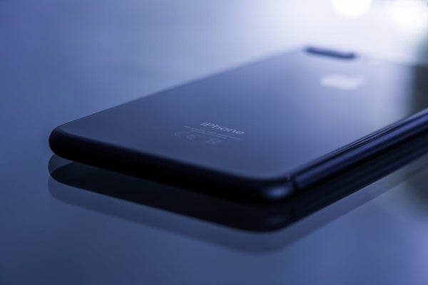 A black iPhone facedown on a black surface. The camera focus is on the bottom end of the phone.