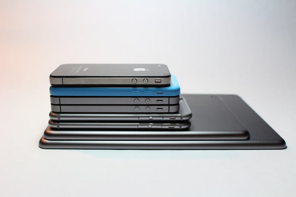 A side view of a stack of different iPhones and iPads. They are stacked with two iPads at the bottom and then recent iPhones through to older iPhones. The iPhone second from the top has a light blue case on. 