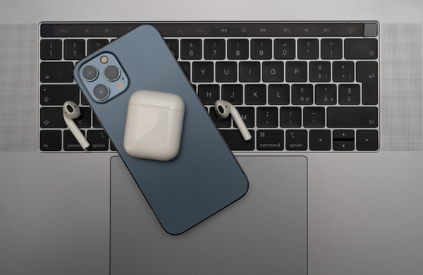 An iPhone facedown on a Mac keyboard with an Air Pod case on top and the Air Pods either side of the iPhone.