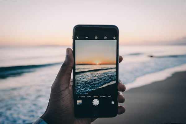 Person holding iPhone taking a picture of the sunset behind the ocean
