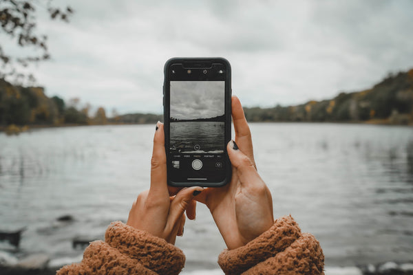 Woman holding up phone taking a photo over a lake