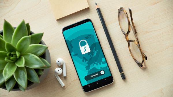 An iPhone with a lock on the display on a wooden desk next to a succulent, pencil, and glasses