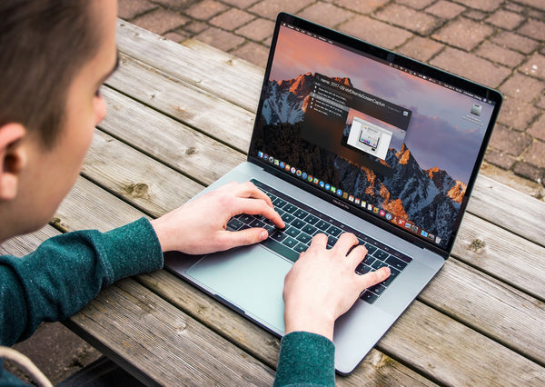 A man typing on a MacBook on a wooden table