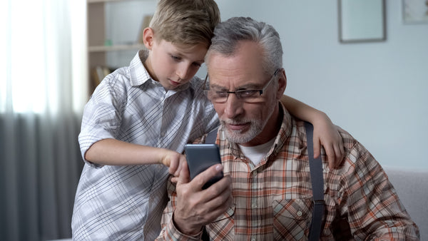 Grandfather being shown how to use a smartphone by grandson