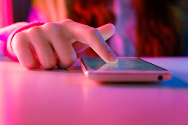 finger pressing on a pink smartphone with a pink glow