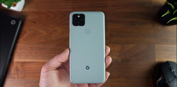 A hand holding a white Google Pixel 5 face down over a wooden table