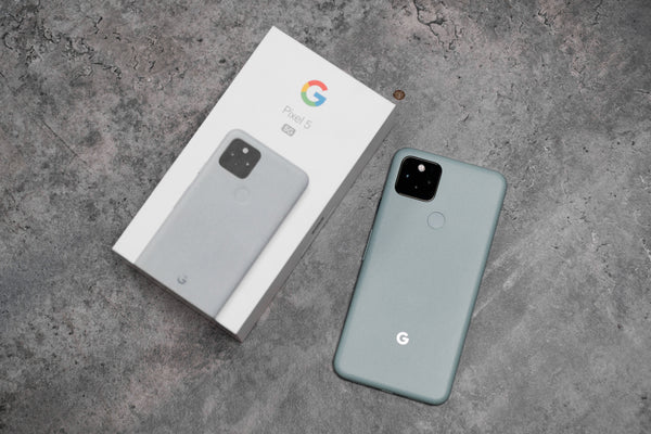 A Google Pixel 5 face down next to its box on a stone grey background