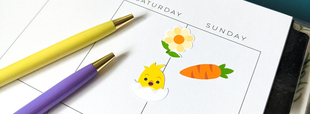 A vertical style blank planner decorated with a flower sticker, a carrot sticker, and a baby chick in an egg sticker. A yellow pen and a purple pen sit on top.