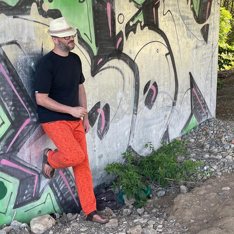 An einem Brückenbetonpfeiler, der das ganze Bild asufüllt und mit grünem und silbernen Graffiti besprüht ist, lehnt auf der linken Seite ein Mann mit schwarzem T-Shirt, Strohhut und selbst genähter Jerseyjogginghose Mr.Haven von mialuna.