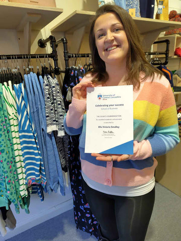 Ella Smalley holding the Dean's Commendation certificate from UCLAN. She is wear a pastel rainbow cardigan from Sugarhill Brighton.