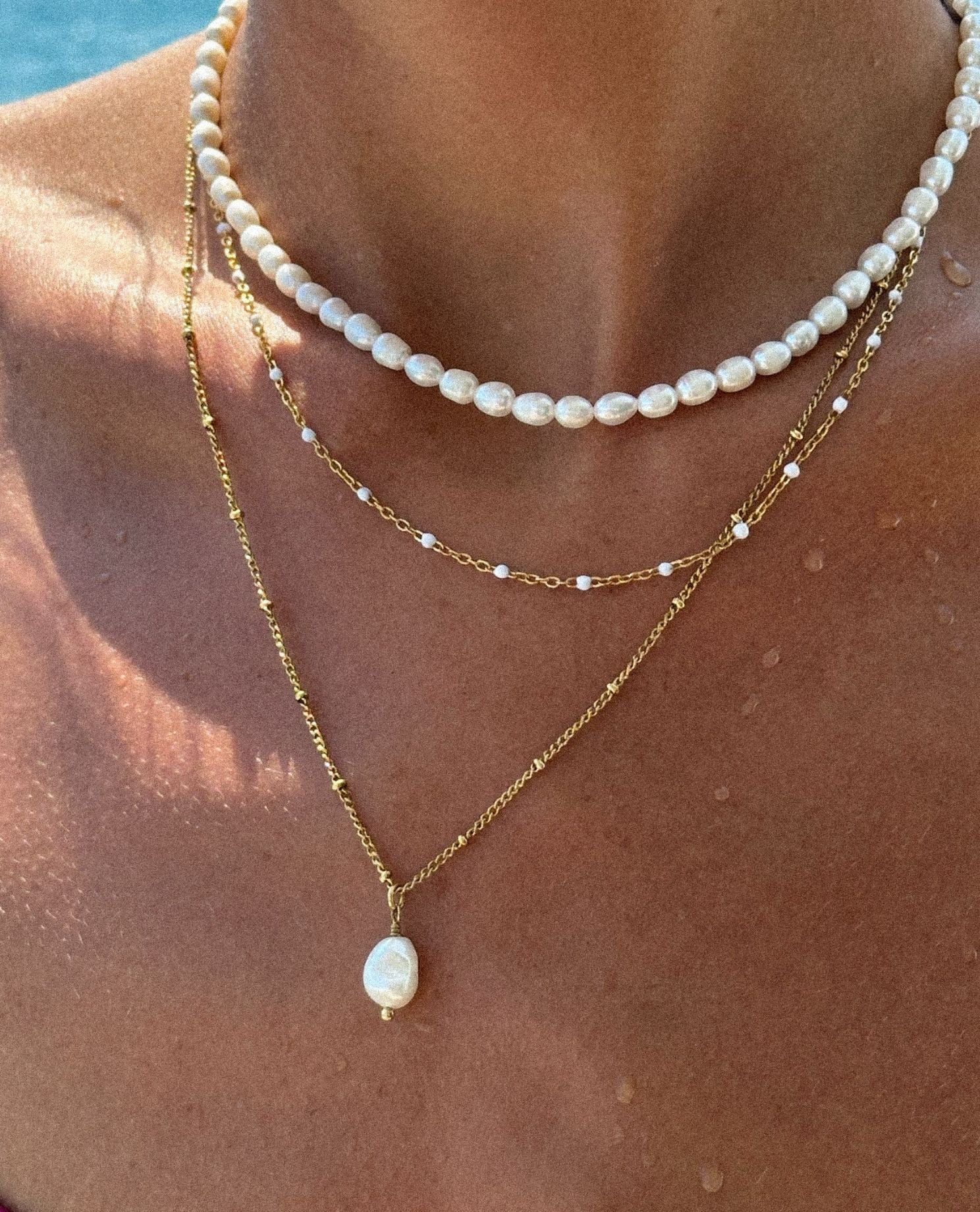 Close-up of layered pearl and gold necklaces on a person's neck.