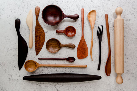 A large variety of different shaped and sized kitchen utensils in various wood grains on a grey specked concrete background