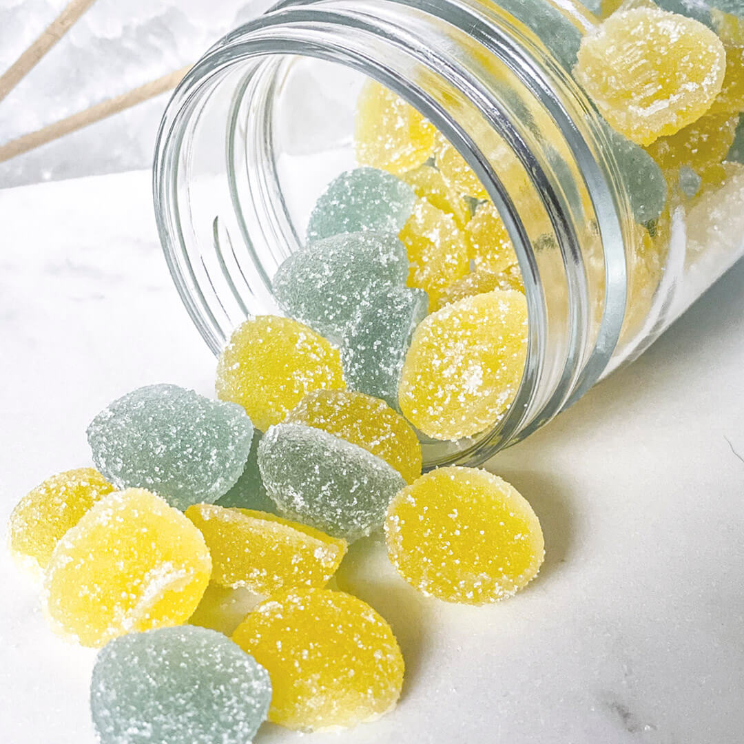 green and yellow gummies in a clear jar spilled on a white table
