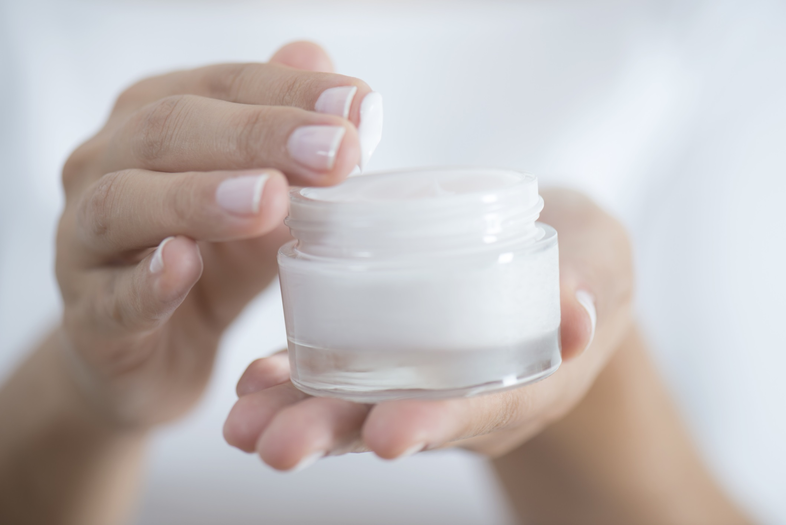 hands holding a moisturizer container and fingers dipped into the cream