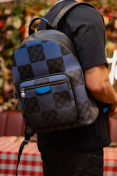 Image of male model holding Louis Vuitton blue and black monogramed back pack.