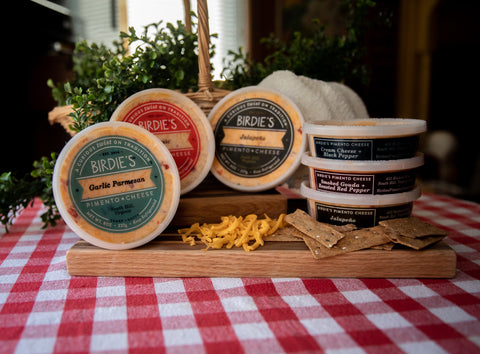 Tubs of Birdie's Pimento cheese on a checkered tablecloth and wooden serving tray