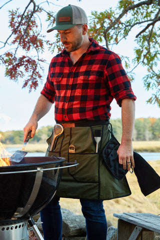Man rocking a flannel shirt + Grill Kilt and standing over an open grill