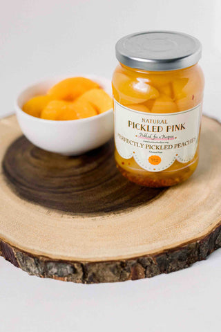 A jar of pickled peaches by Pickled Pink Foods with dried peaches on wood