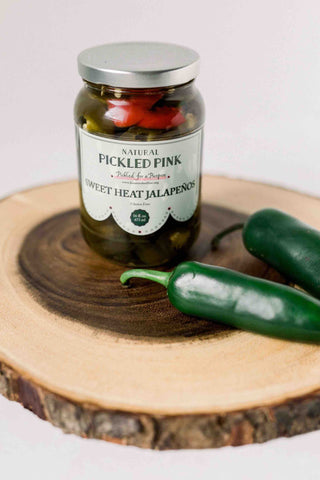 A jar of pickled jalapeños by Pickled Pink Foods with jalapeños on wood