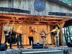 The Blue Water Ramblers performing on an open-air stage in front of a wooden building.