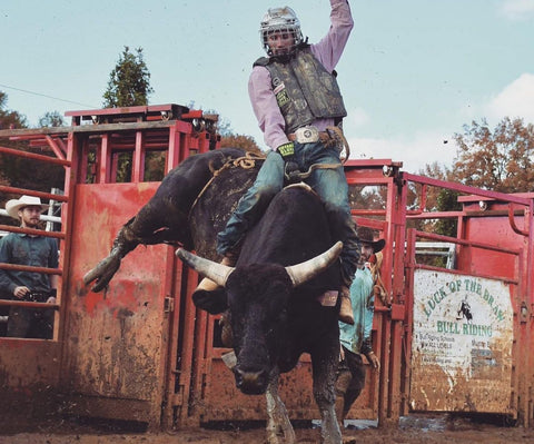 Cowboy riding a bucking bull, while wearing his custom belt buckle from Cowboss Silversmiths