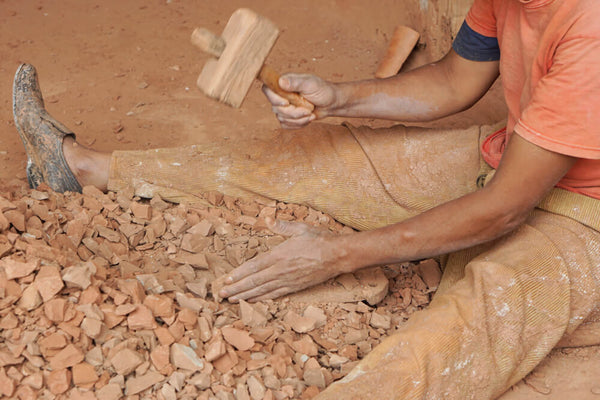 Artisan breaking up clay rock for ceramic goods.