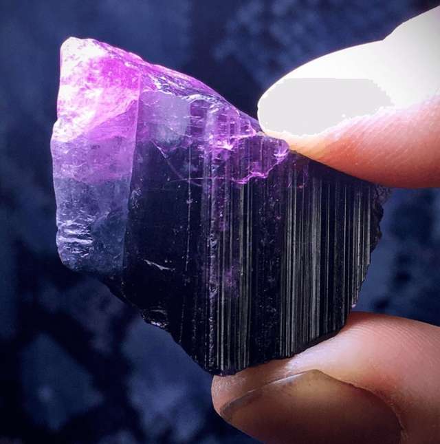 two fingers holding tiny piece of purple unpolished crystal rock