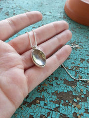 hand holding a silver necklace with an oval pendant