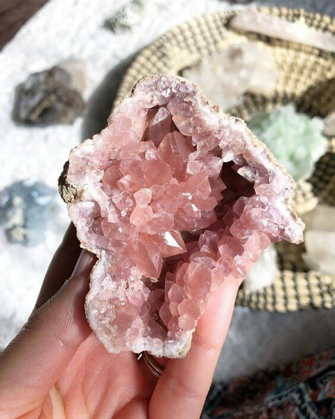 hand holding raw pink amethyst crystal with other rocks as background