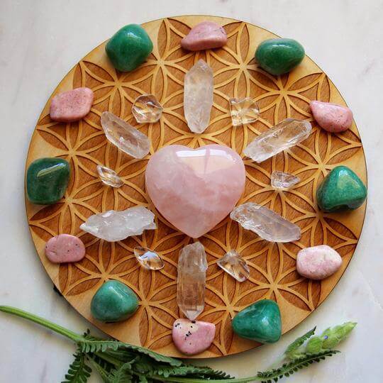 pink green white clear crystal rock and smooth gem stones arranged on a circle woodensurface