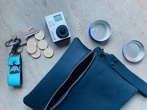 Mindful Manta neoprene pouch in black surrounded by adventure camera, keyring, loose change and lip balm.