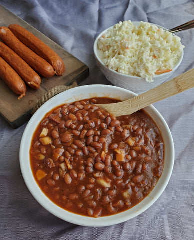 a full bowl of Slow Cooker Baked Beans with sausage links and a spread nearby