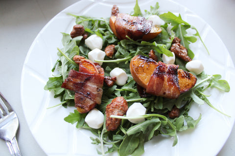 Bacon wrapped grilled peaches top an arugula salad