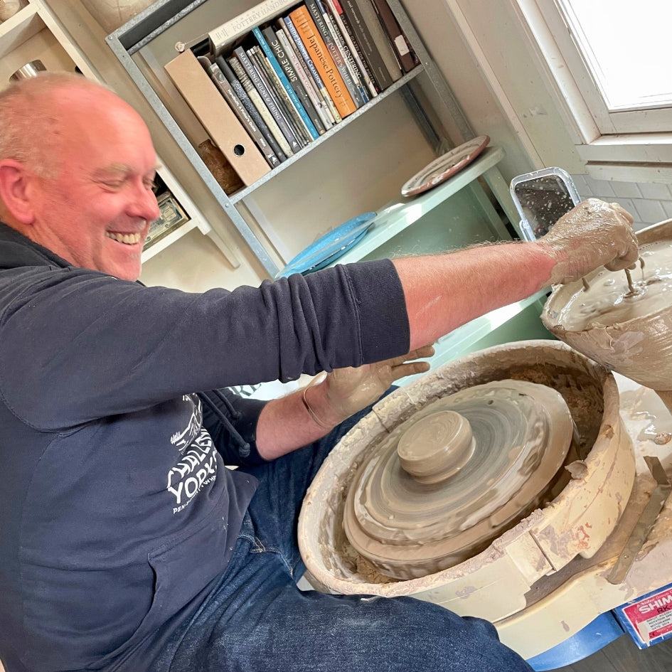 Male pottery student sitting in front of a potter's wheel throwing a bowl in Sabine's Devon Studio.