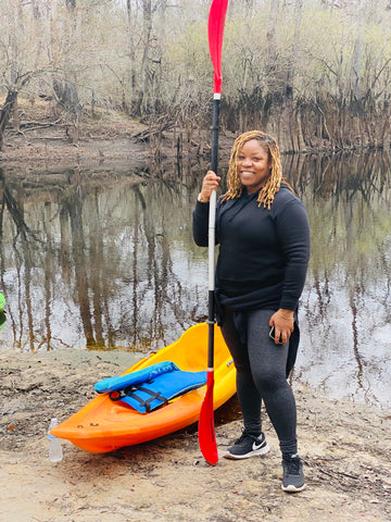 Black woman standing next to a kayak