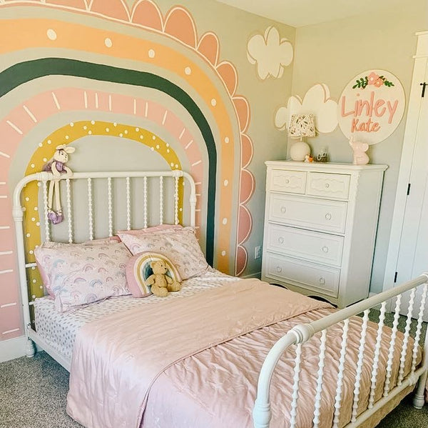 A little girl's room with a rainbow mural painted over the bed frame with yellow, navy, and pink colors