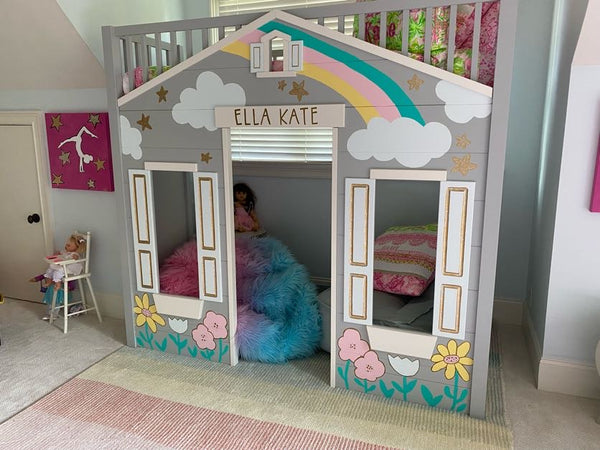 A play house kids reading nook inside of a child's room with a rainbow painted above the door, and other various painting decorations around, including flowers under the windowsills