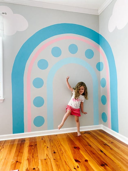 A little girl balancing in front of a rainbow wall mural made up of cotton candy blue and pink