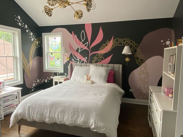 A dark grey wall with hand-painted pink and gold wall art of leaves and stylized rainbows