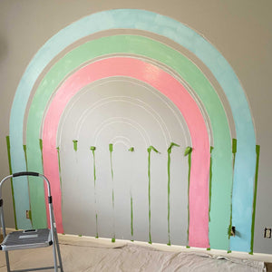 Half way through painting E's rainbow mural. The chalked out guidelines are still visible, but the first coat of sky blue, soft green, and warm pink are in place.