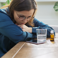 Woman looking at her phone with water and oils nearby, trying to figure out if she has estrogen dominance