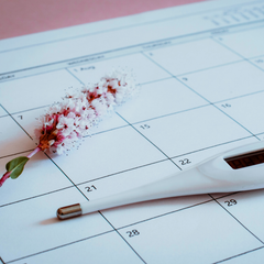 basal body thermometer sitting on a calendar, being used for fertility awareness