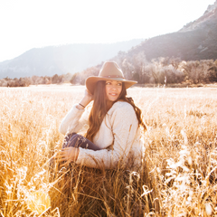 Woman sitting in a field below the mountains with the sun shining down on her