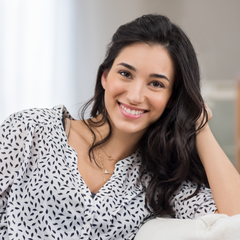 woman sitting on a couch, leaning into the back of it with her head propped on her arm while smiling