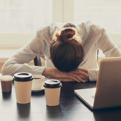 Tired, stressed woman with 4 cups of coffee in front of her at her workspace