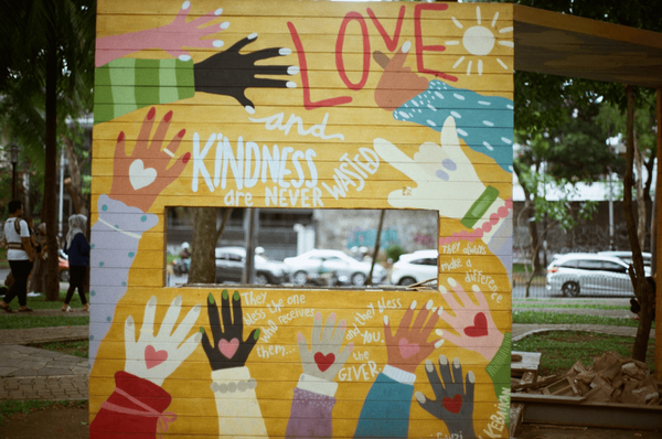 A wall with painted hands that says "Love and kindness are never wasted".